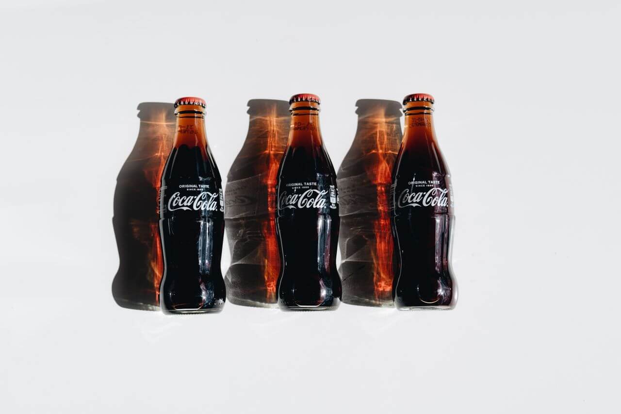 Three glass Coca-Cola bottles casting artistic shadows on a bright surface.