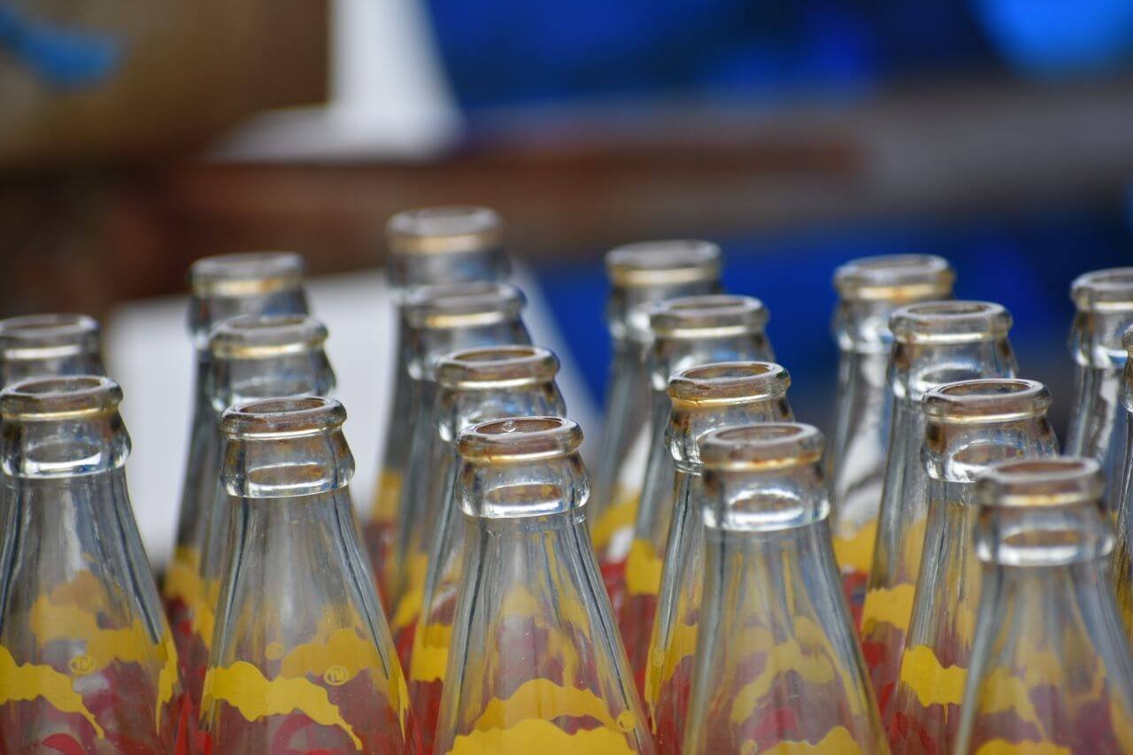 Empty glass soda bottles arranged in rows with colorful labels, perfect for recycling themes.