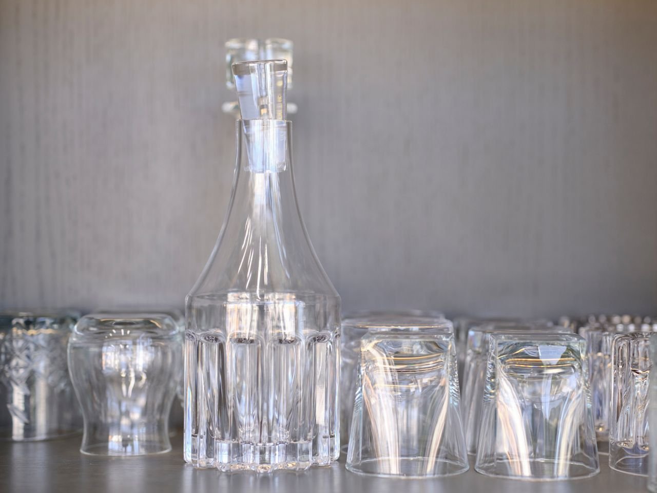 Detailed shot of a clear glass pitcher surrounded by upside-down glasses on a shelf.