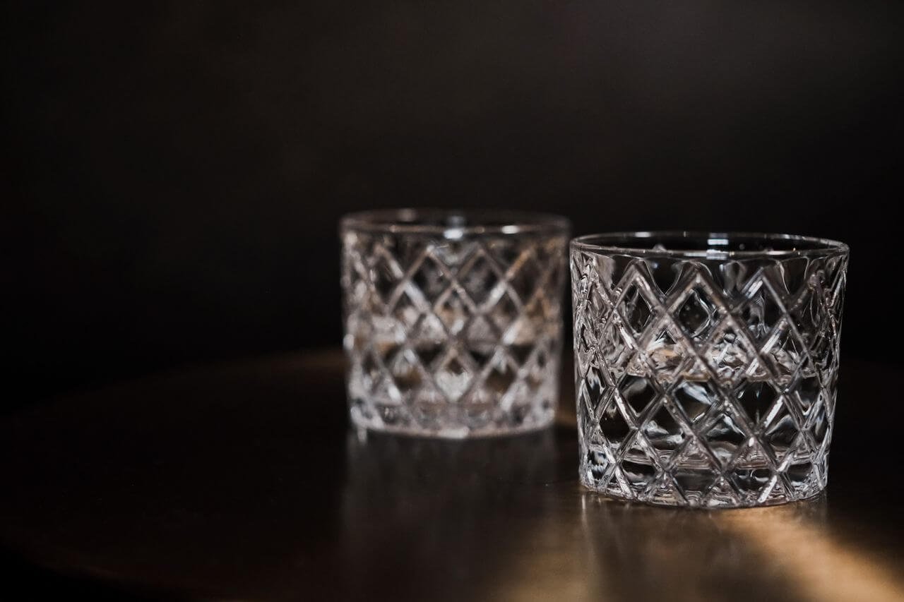 Two crystal glasses on a dark surface with moody lighting