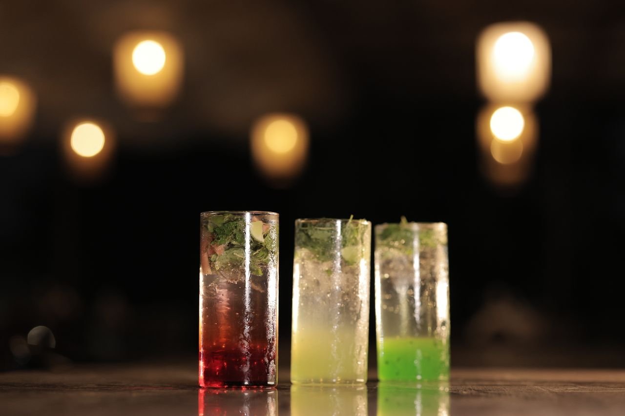 Three colorful cocktails with mint garnishes in a dimly lit bar setting.