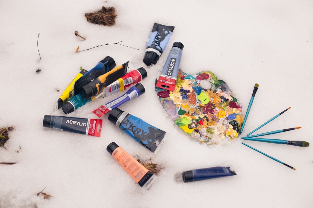 Colorful acrylic paint tubes and palette with brushes lying on a snow surface, artistic winter theme.