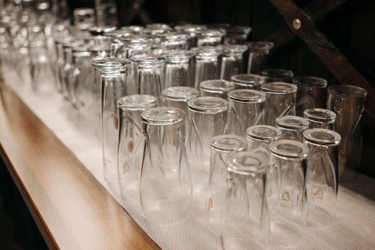 A neat arrangement of upside down drinking glasses on a wooden shelf in a dimly lit setting.
