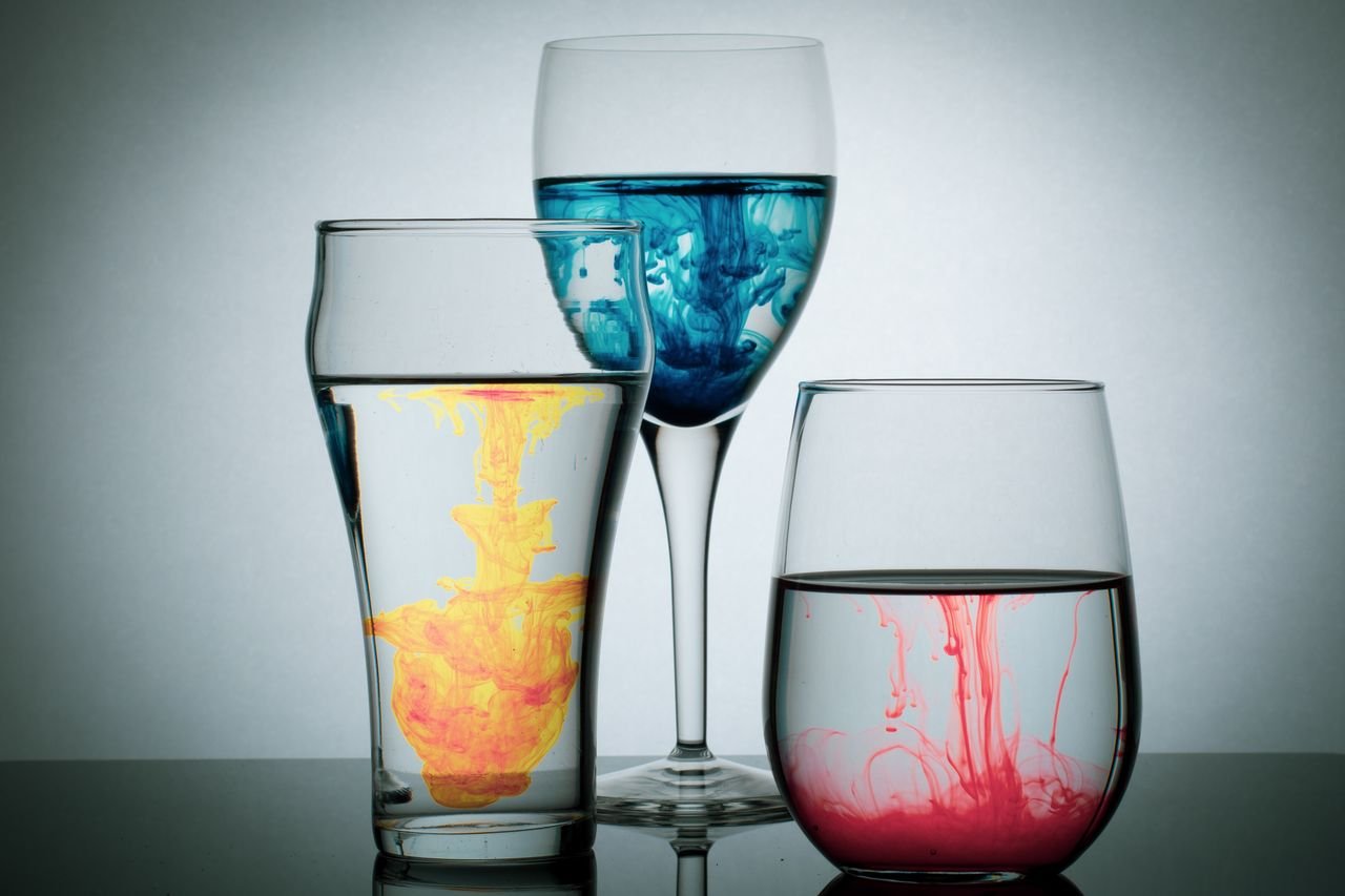 Vibrant acrylic paint swirling in glasses creating mesmerizing patterns against a neutral backdrop.