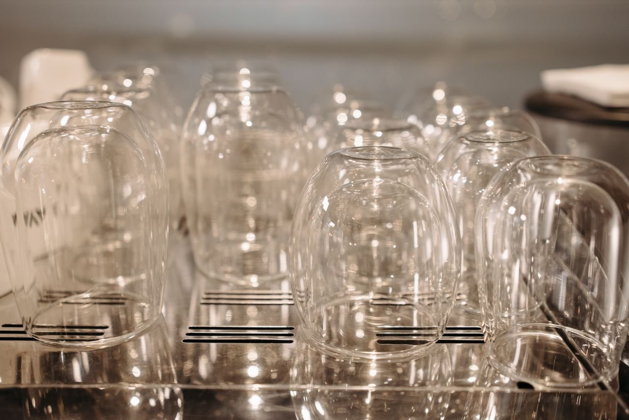 A collection of upside-down glasses drying on a stainless steel rack with soft lighting.