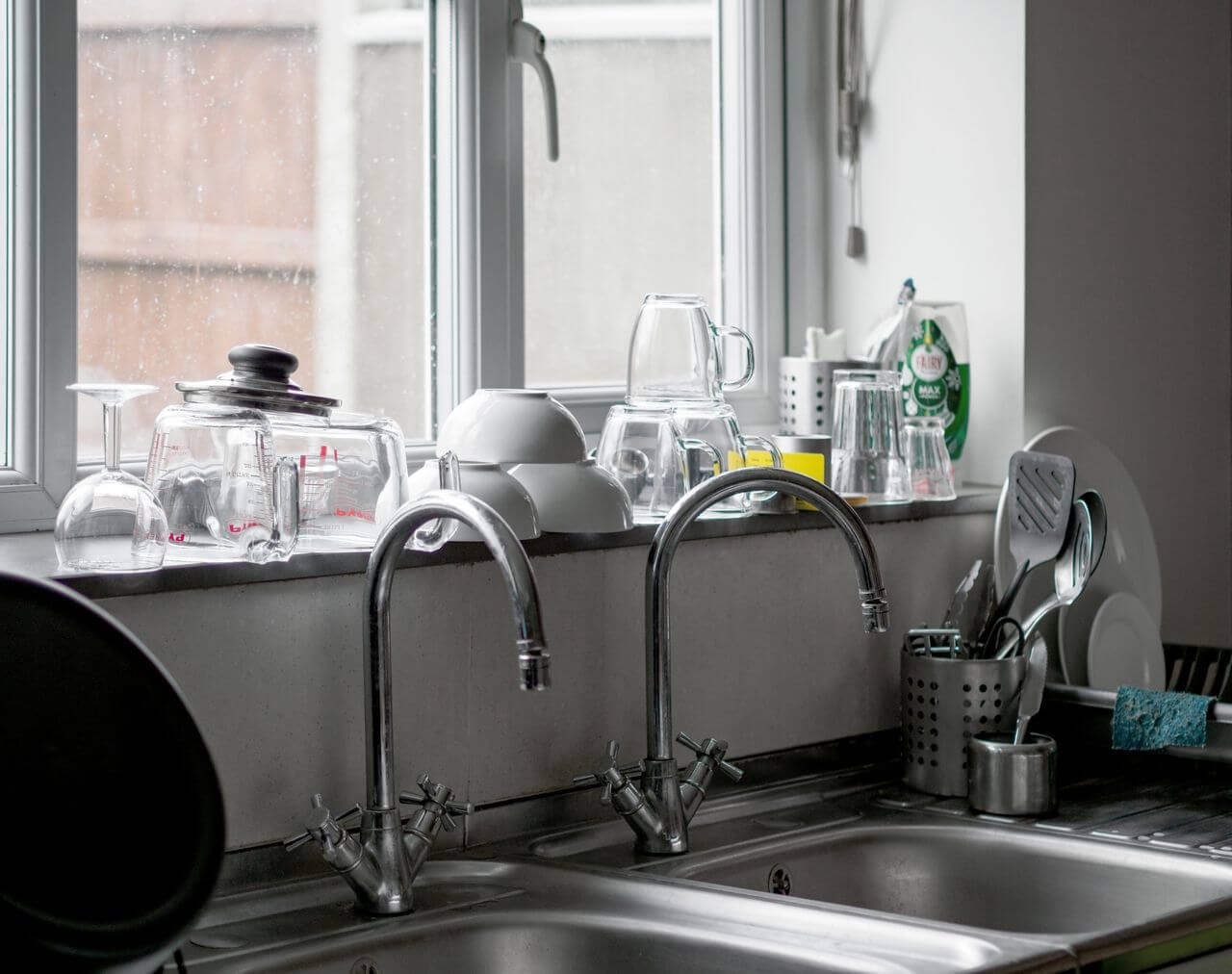 Contemporary kitchen featuring a stainless steel sink with kitchenware and glassware on the windowsill.