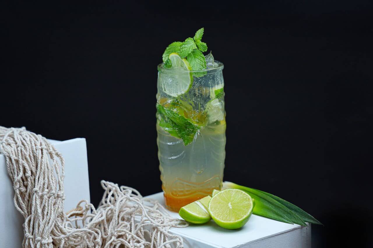 A highball glass filled with a refreshing mint lime mojito, garnished with fresh mint and lime slices on a black background.