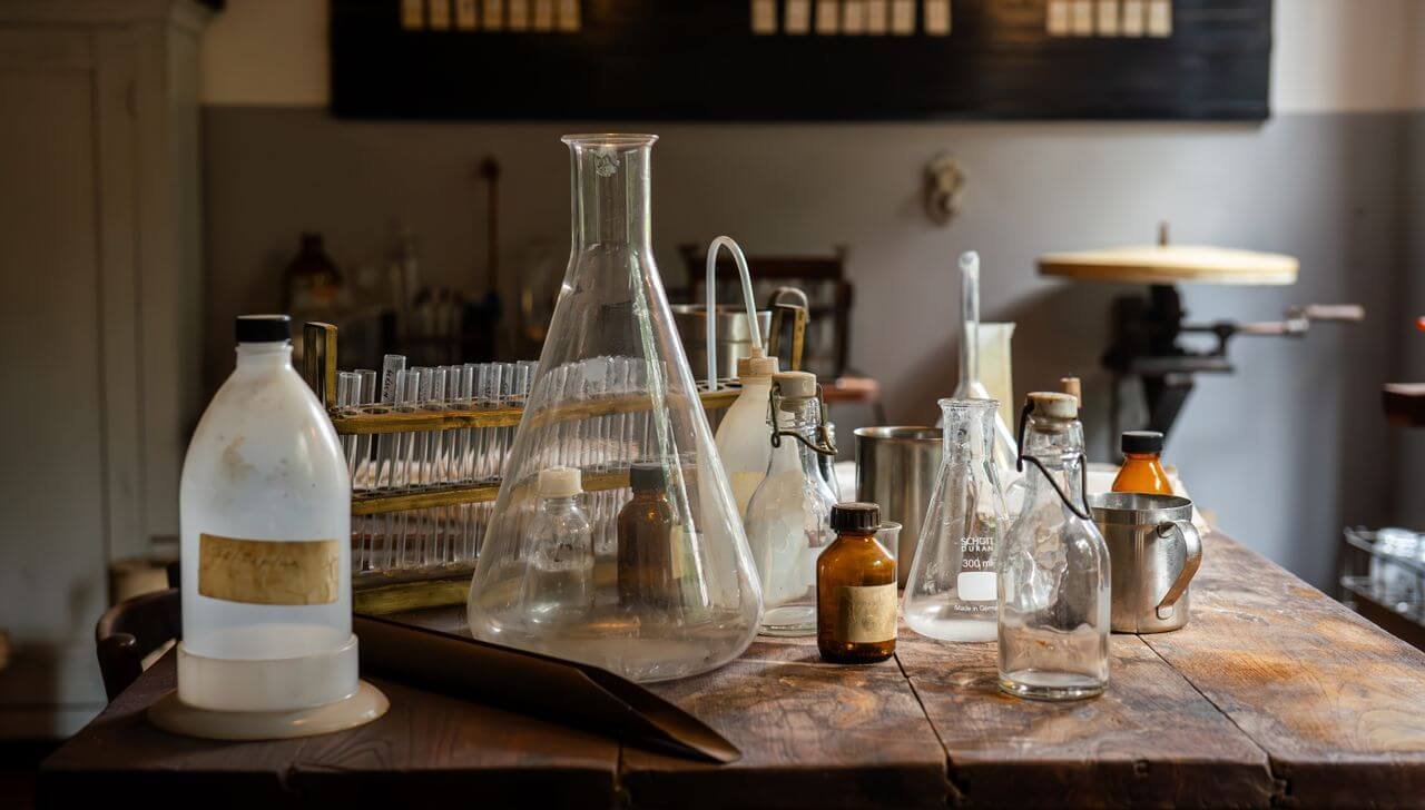 A rustic chemistry lab featuring an array of glassware, flasks, and test tubes on a wooden table.