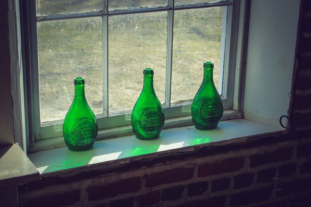 Three vintage green glass bottles placed on a sunlit window sill, casting reflections.