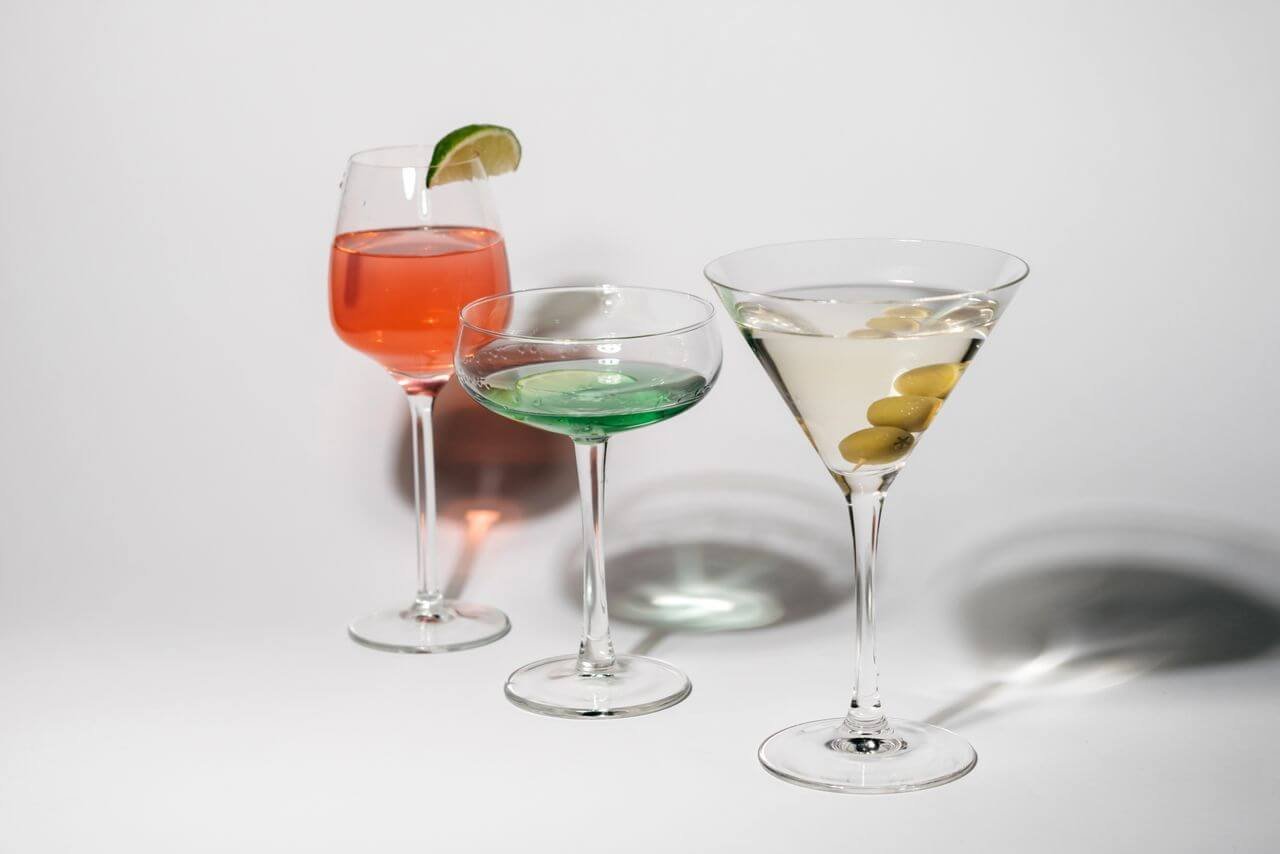 Stylish arrangement of pink, green, and clear cocktails in glasses with lime and olive garnishes.
