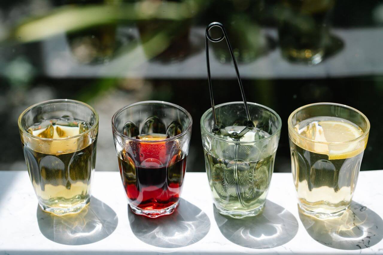 Four glasses of iced beverages in sunlight, showcasing colorful drink variety.