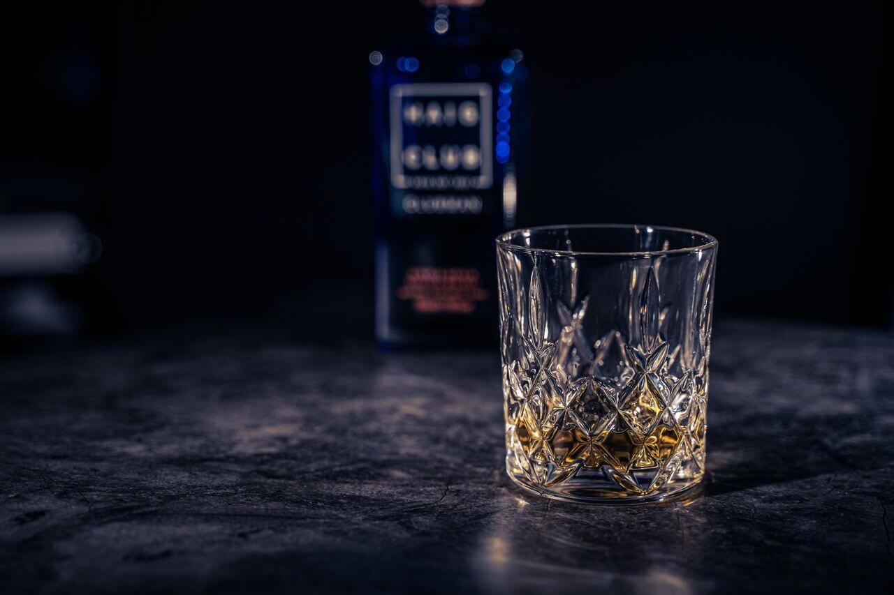 Close-up of whiskey in a crystal glass on a rustic table with a blurred background.