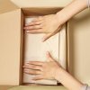 Close-up of hands packing a cardboard box with care using parchment paper.